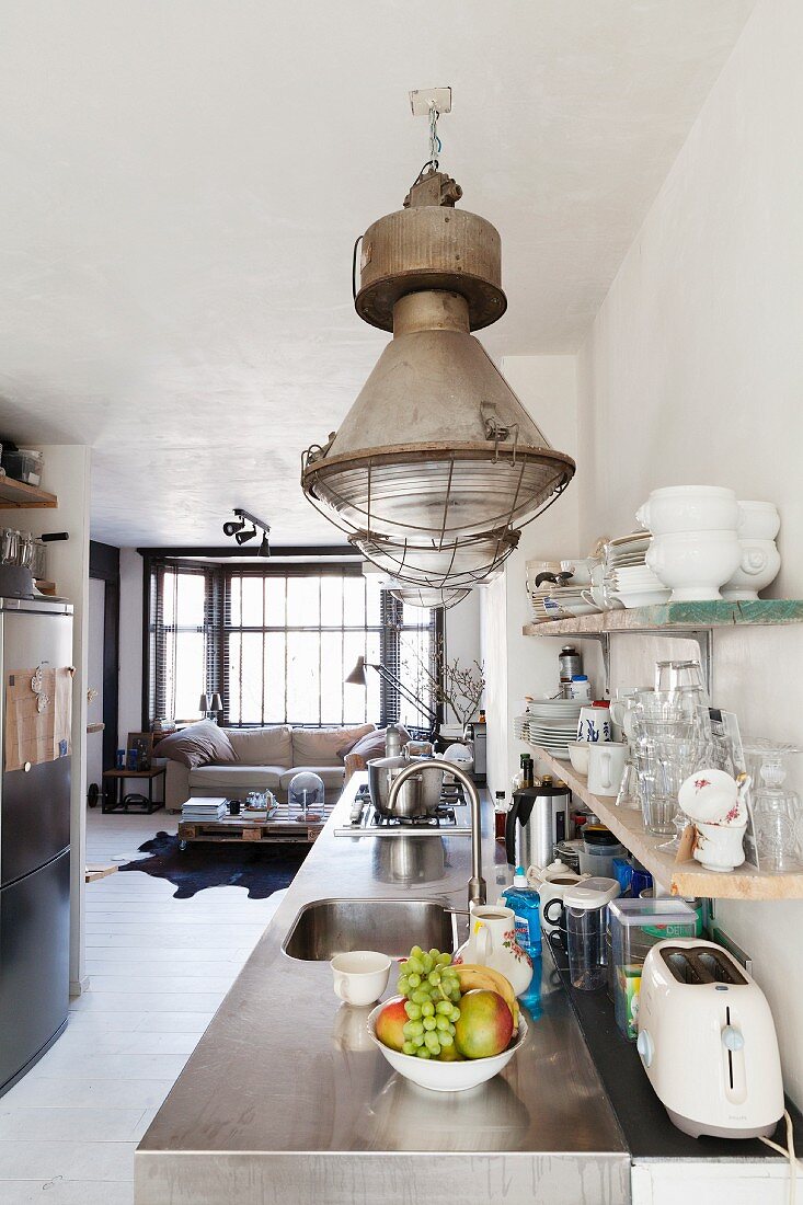Kitchen counter with stainless steel worksurface below industrial-style pendant lamps in open-plan interior