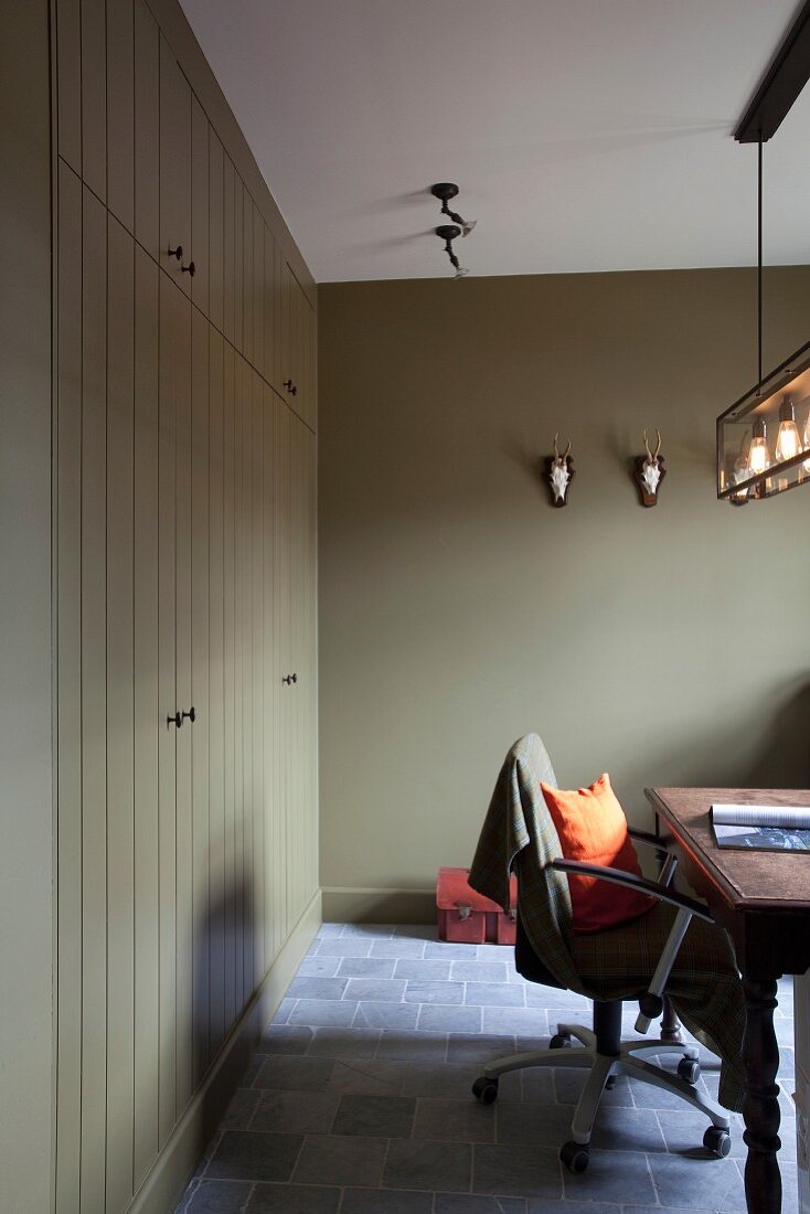 Rustic, olive-green study with stone floor and wooden fitted cabinets