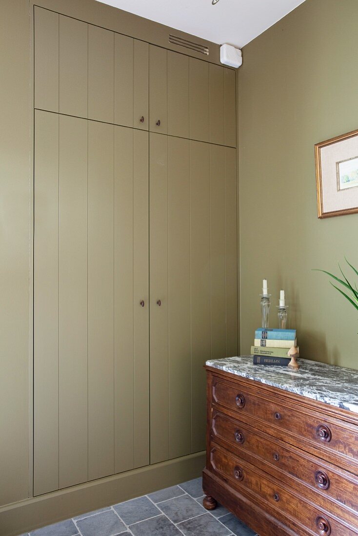 Antique chest of drawers with stone counter in front of wooden fitted cupboard