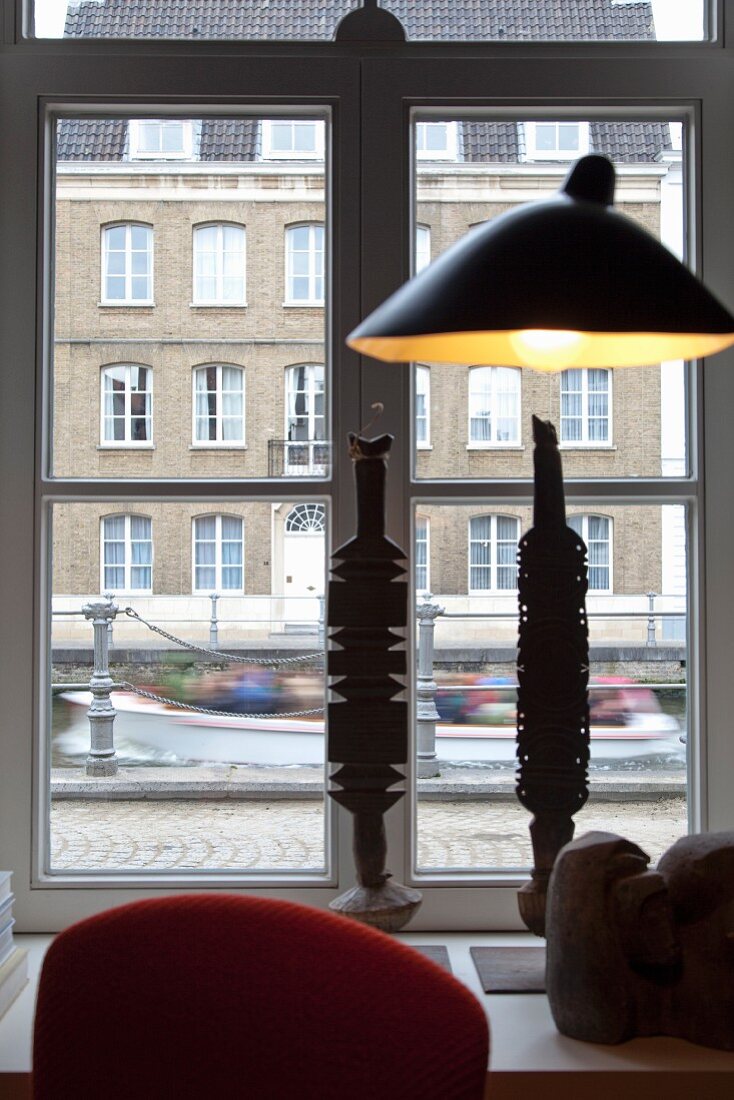 Lampenschirm von Serge Mouille vor Fenster mit Blick auf Altbau Gebäude und Gracht, auf Fenstersims Kunstobjekte aus Metall