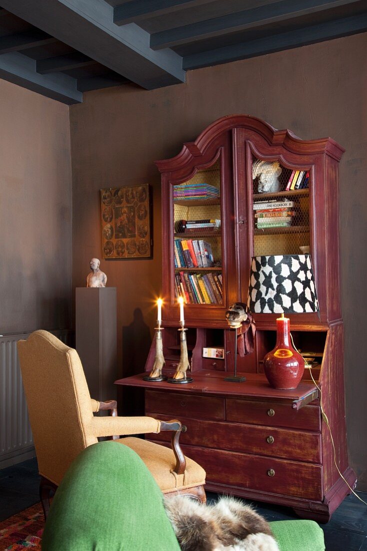 Pastel green armchair in front of lit candles on antique bureau against dark wall