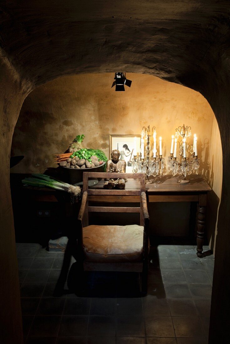 Crystal candelabras, Buddha figurine and bowl of vegetables on wooden table under spotlight in vaulted cellar