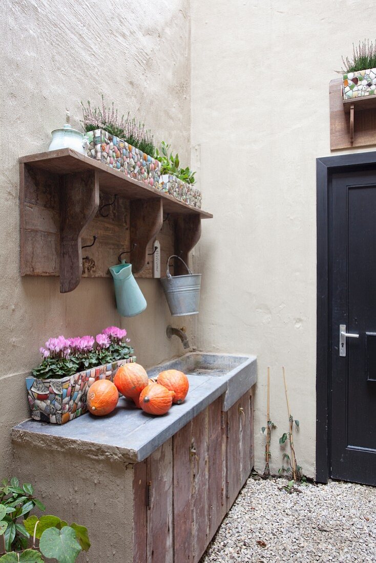 Rustic vintage sink unit in courtyard decorated with pumpkins and windowbox of cyclamen