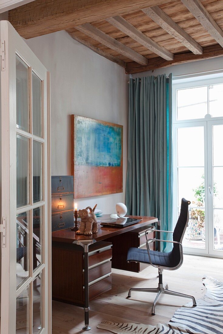 Blick auf Retro-Schreibtisch und Klassiker Bürostuhl in Wohnraumecke mit rustikaler Holzdecke