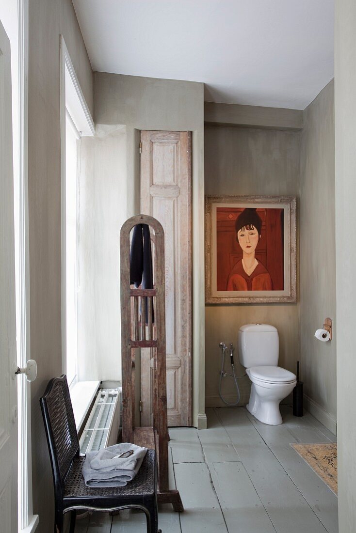 Antique chair in vintage bathroom with white toilet in niche painted pale grey and portrait of woman in shades of red