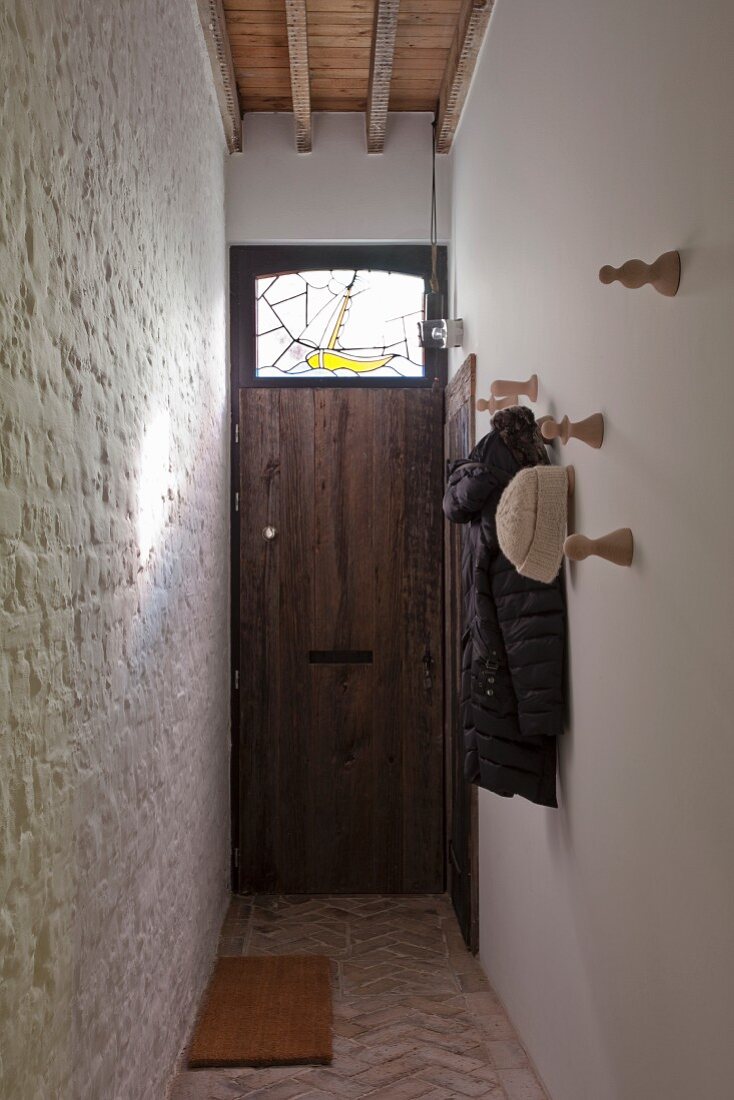 Schmaler Hausgang mit Steinbelag in Fischgrätmuster auf Boden, geweisselte Ziegelwand und Garderobenhaken aus Holz