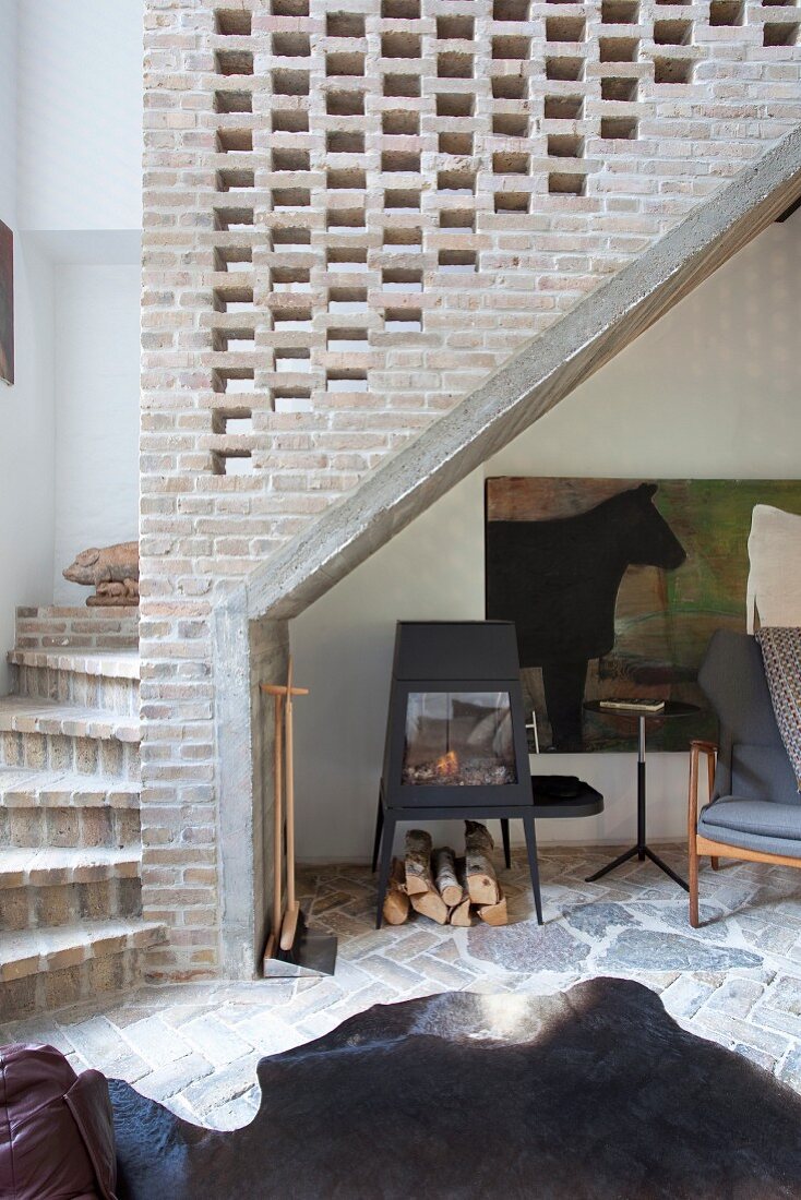 Animal-skin rug on stone floor below winding staircase with perforated brick side wall
