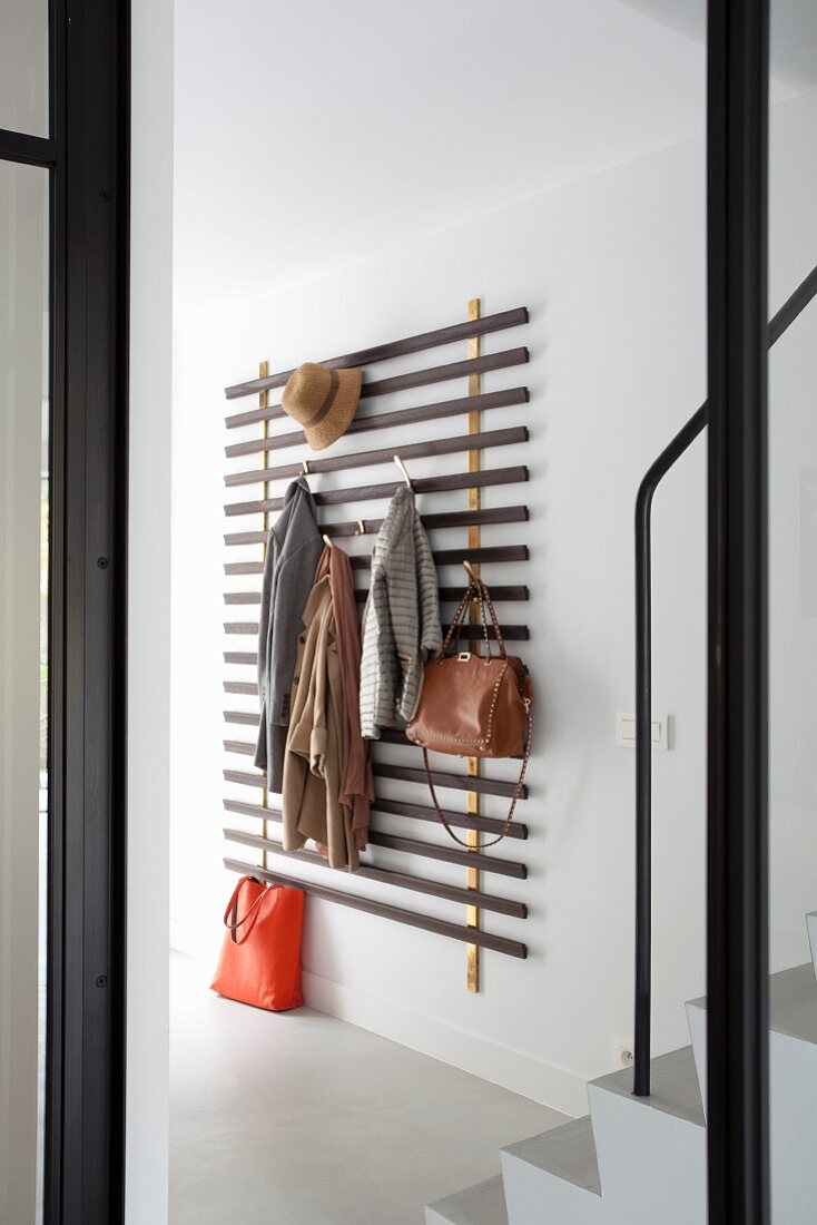 Clothes hung from minimalist coat rack made from wooden slats in modern hallway