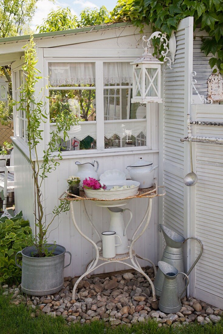Vintage Waschschüssel und Krug in rostigem Metallgestell vor Gartenhäuschen