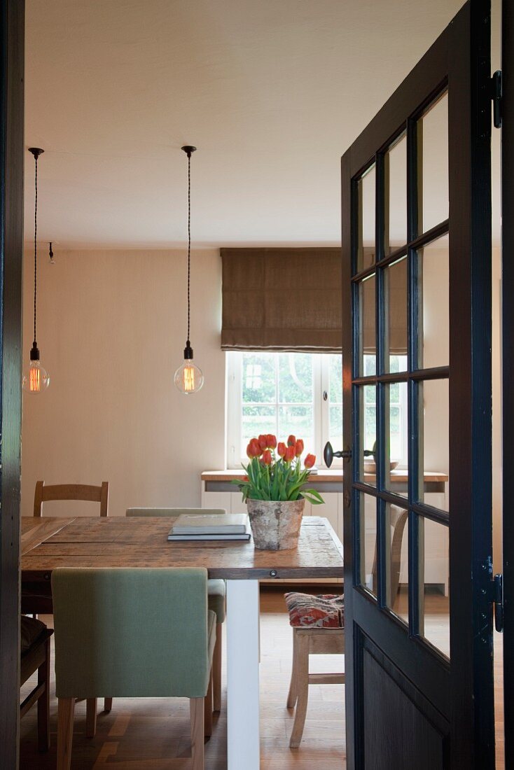Blick durch geöffnete Tür mit Sprossen auf Esstisch mit verschiedenen Stühlen