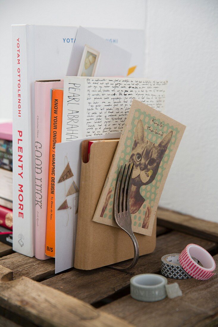 Selbstgebastelte Buchstütze mit gebogener Vintage-Gabel, verschiedene Bücher und Masking-Tape auf Holzunterlage