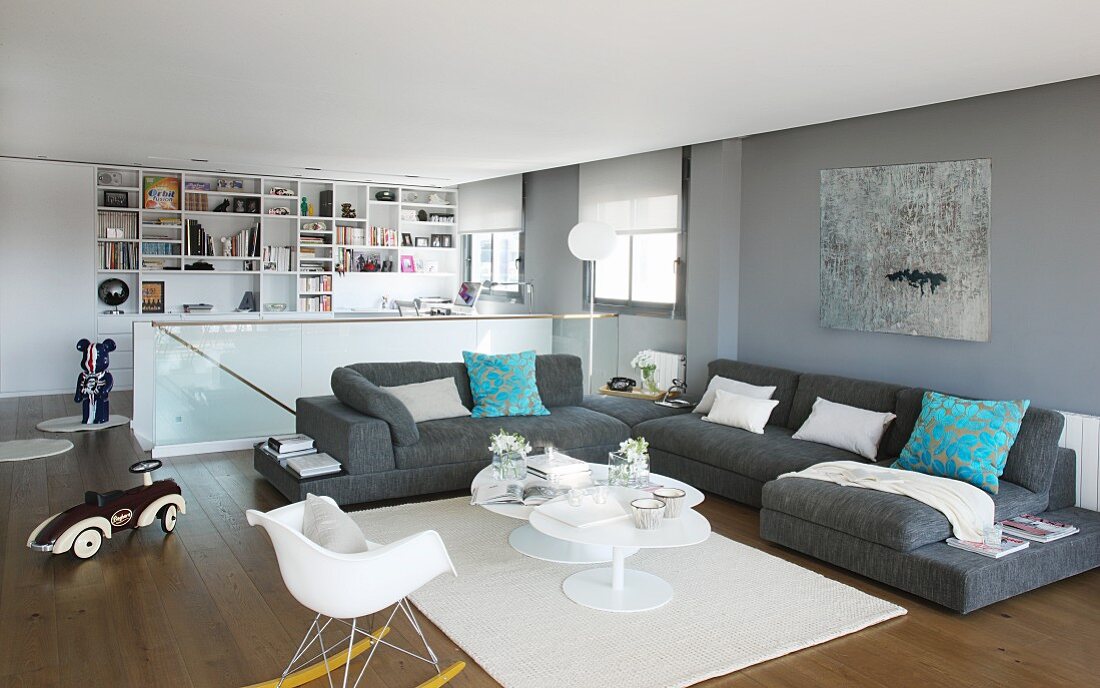 Modern, grey and white interior with large sofa combination; maisonette staircase and fitted shelving in background