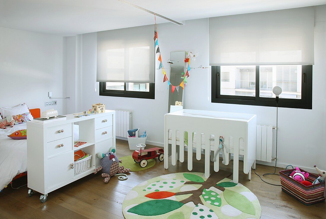 White furniture and colourful elements such as round rug with stylised tree motif in modern child's bedroom