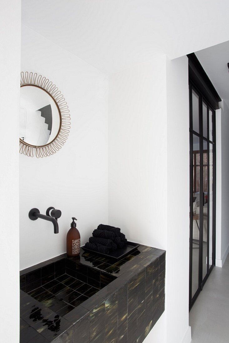 Waschtisch mit schwarzen marmorierten Fliesen unter rundem Spiegel im Badezimmer