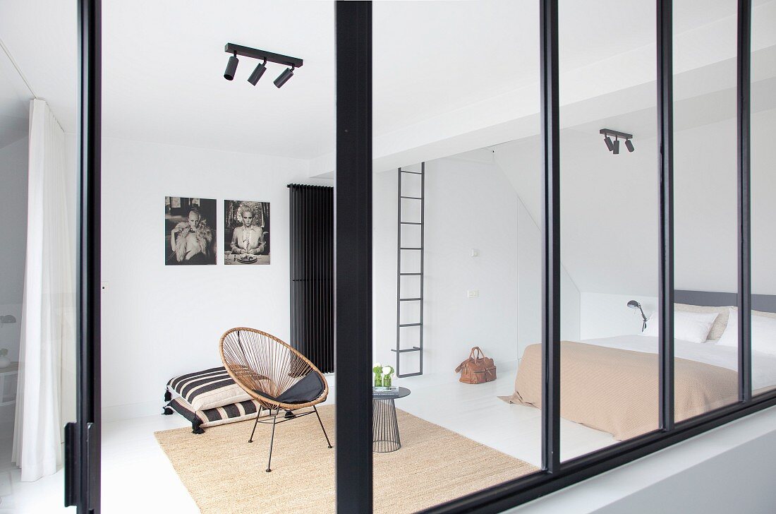 Blick durch Innenfenster mit schwarzem Metallrahmen in minimalistisches Schlafzimmer