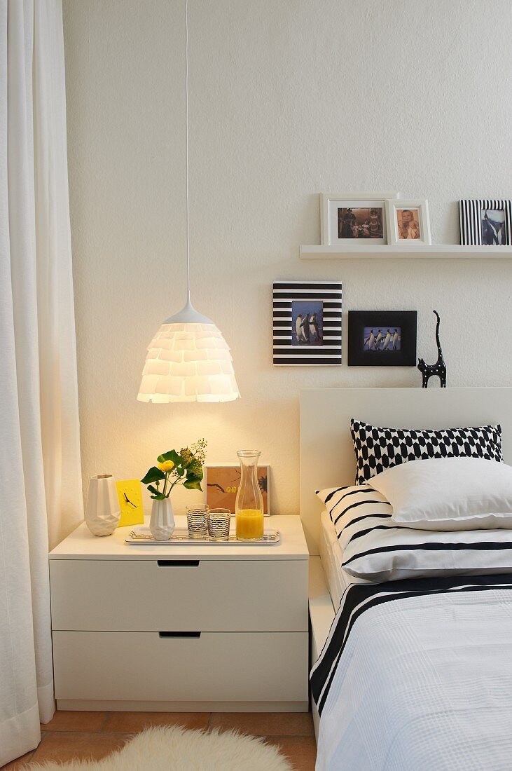 Mixture of black and white patterns on bed and wall; warm light from pendant lamp with layered lampshade above bedside cabinet