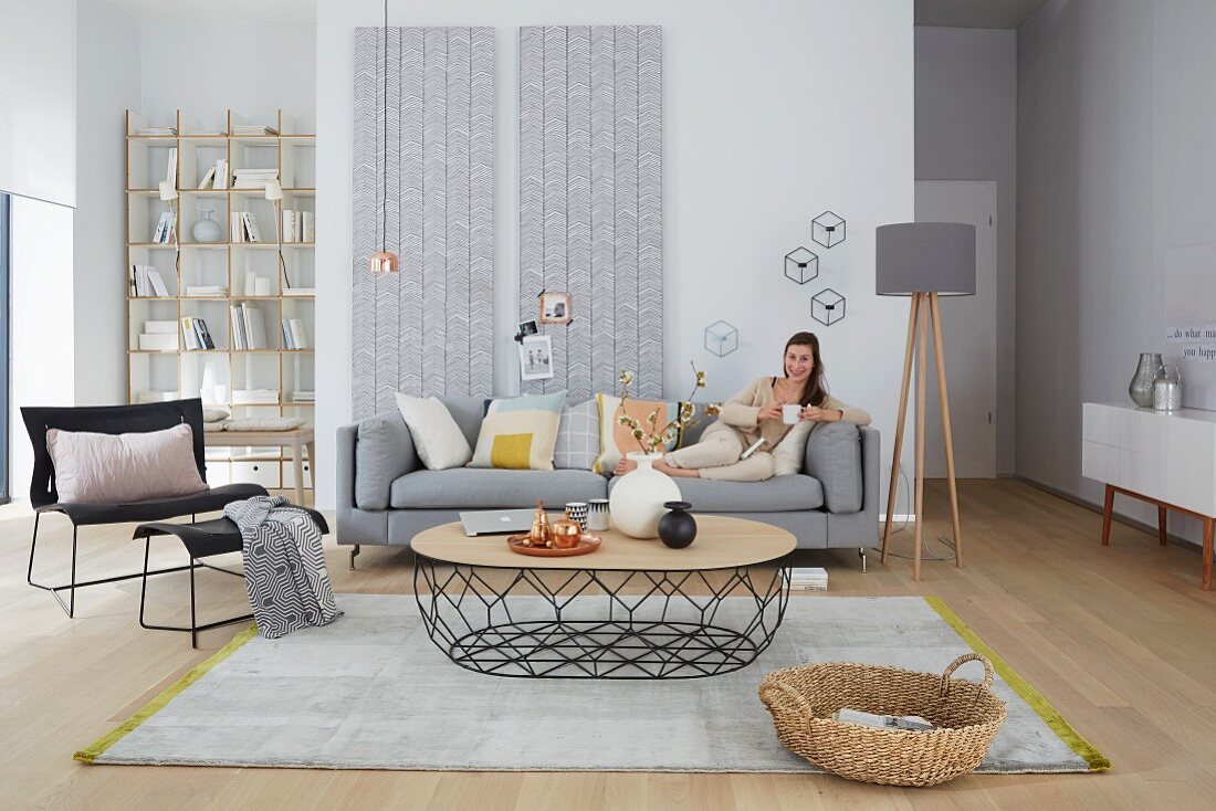 A woman reading on a sofa in a seating area in light grey tones with copper accents against wallpapered wood panels
