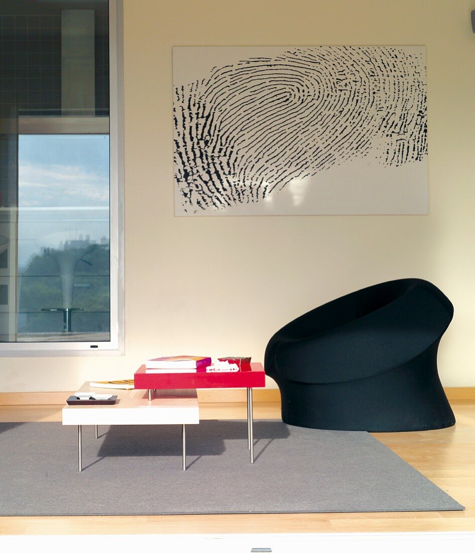 Colourful set of coffee tables and black easy chair on grey rug below black and white artwork on wall