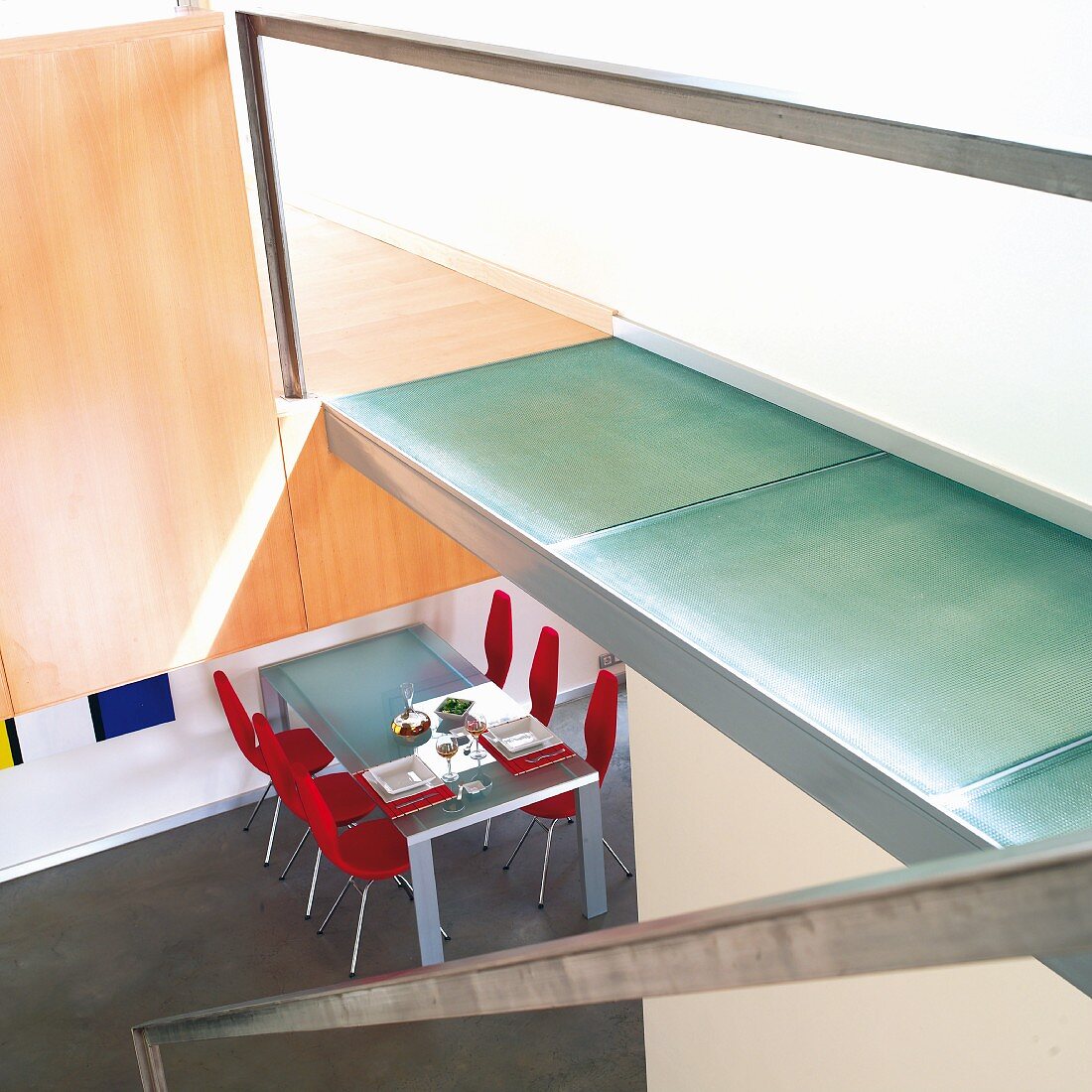 Treppe mit Steg an der Seite, auf Boden Glaspaneelen, Blick in offenen Essbereich mit Tisch und roten Stühlen