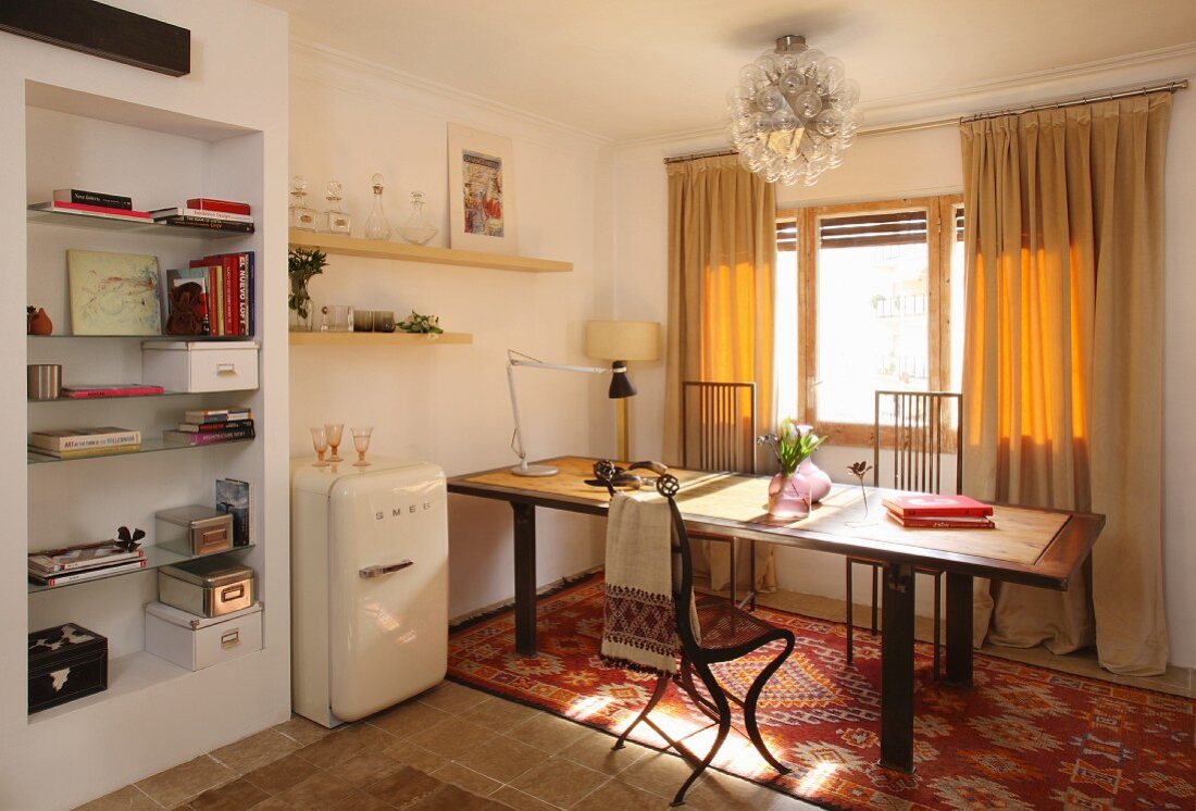 Dining area below window with yellow, floor-length curtains, fifties fridge next to protruding wall section with fitted shelving
