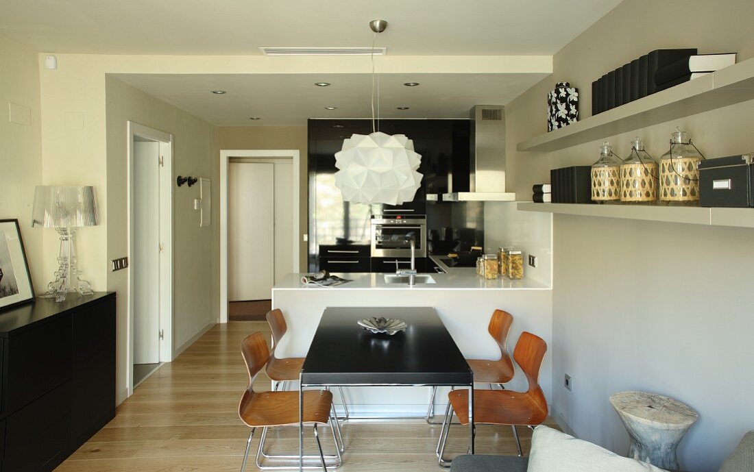 Table with black top and wooden shell chairs in front of counter in open-plan kitchen