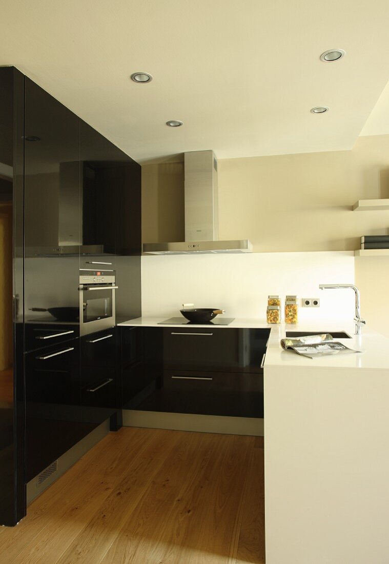 White kitchen counter and fitted cupboards with glossy, black fronts in open-plan kitchen
