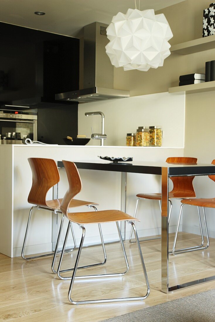 Designer-Hängeleuchte über Tisch und Schalenstühle mit Retro Flair, daneben monolithische Theke in Weiß in offener Küche