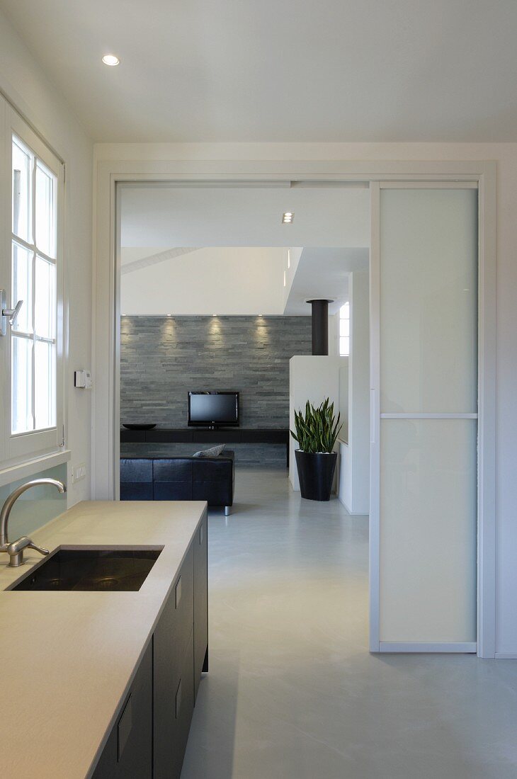 Küchenzeile am Fenster, vor offener Schiebetür und Blick ins moderne Wohnzimmer