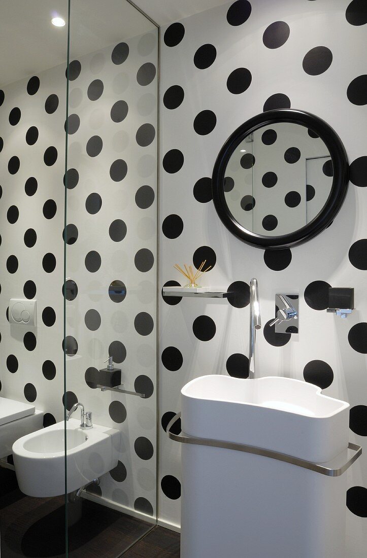 Designer Waschbecken vor schwarz-weiss gepunkteter Wand, seitlich Glas Trennscheibe vor Bidet und Toilette