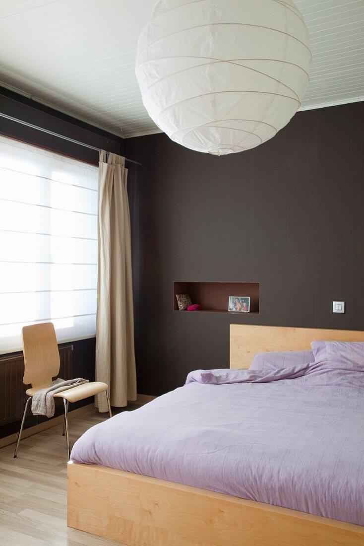 Doppelbett mit fliederfarbener Bettwäsche, in dunkelbraun getöntem Schlafzimmer