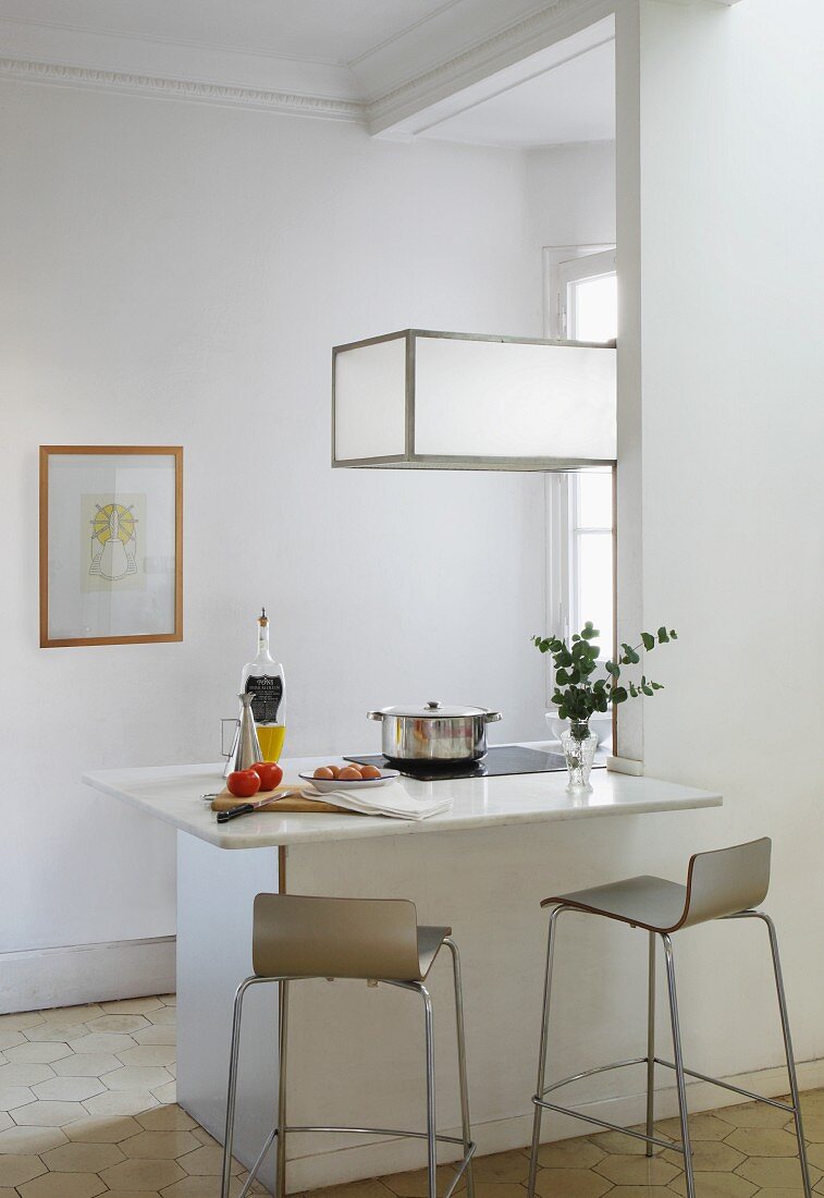 Designer bar stools at counter with white stone counter below cubic pendant lamp in minimalist interior