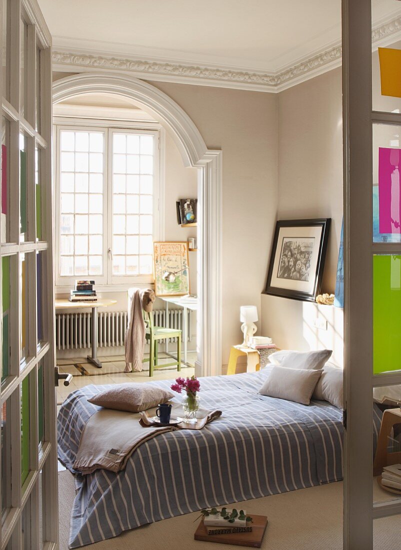 Blick durch offene Tür ins Schlafzimmer, gestreifte Tagesdecke auf Doppelbett, im Hintergrund Durchgang mit Rundbogen