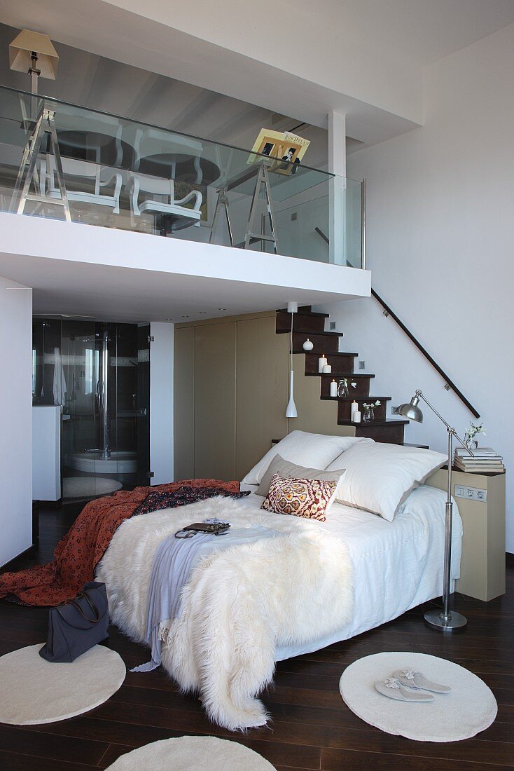Round rugs on dark parquet floor in front of double bed; ensuite bathroom below mezzanine reached by narrow staircase
