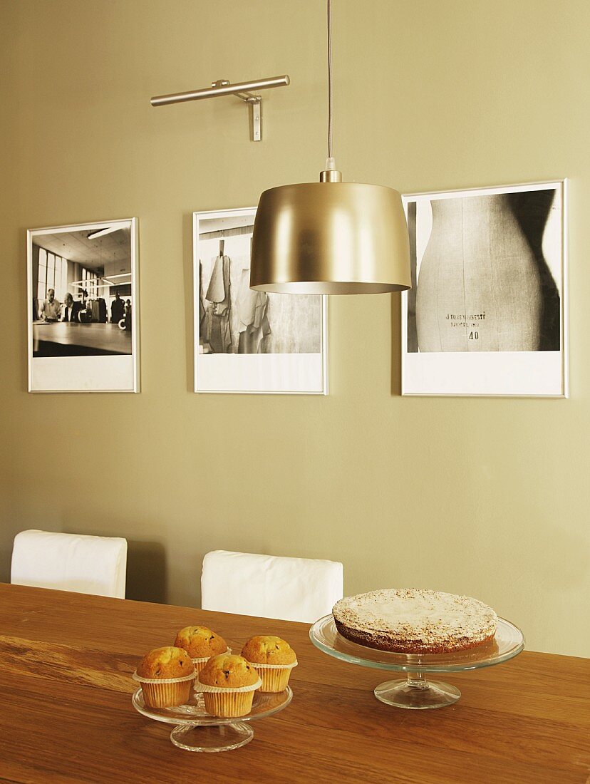 Muffins and cake on dining table; pendant lamps with metal lampshades and artistic black and white photos on wall