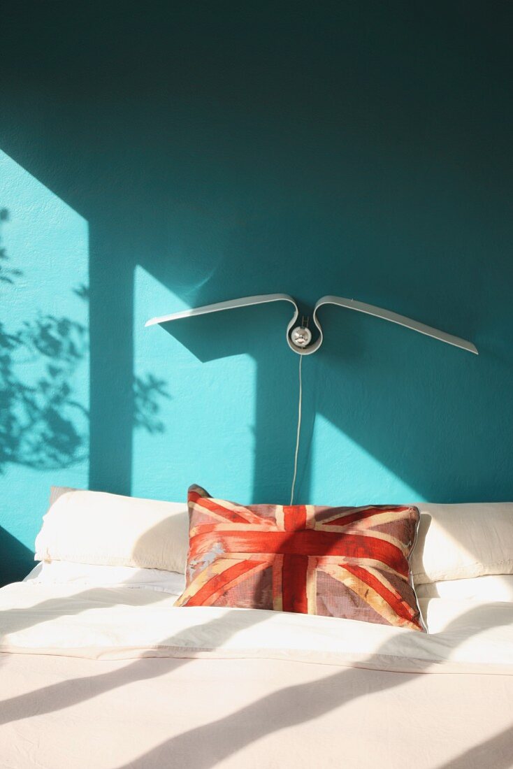 Union flag scatter cushion on double bed below seagull-shaped lamp on wall painted turquoise