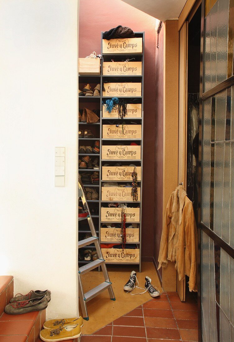 Schuh- und Kleidungsregal mit Schüben aus französischen Weinkisten in kleinem Lagerraum; Schuhe auf Treppenstufen mit Terracottafliesen im Vordergrund