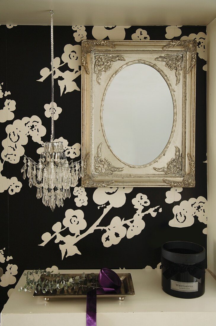 Antikspiegel und Mini-Kronleuchter über der Ablage einer Garderobe; florale schwarz-weiße tapete als Hintergrund