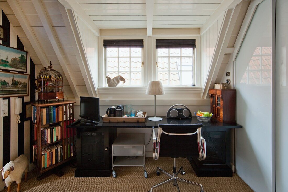 Schreibtisch mit Drehstuhlklassiker von Eames, antiken Kleinmöbeln neben Bücherregal im Dachzimmer