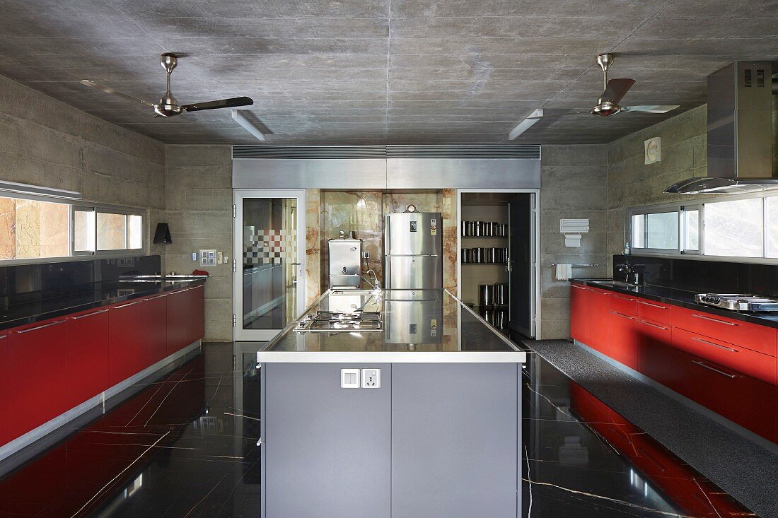 Island counter between kitchen counters with red fronts; stainless steel fridge in background