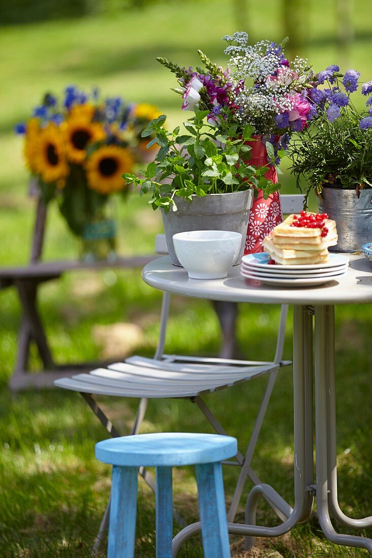 Blumenstrauss, Pflanztöpfe & Tellerstapel mit Waffeln auf Tisch im sommerlichen Garten