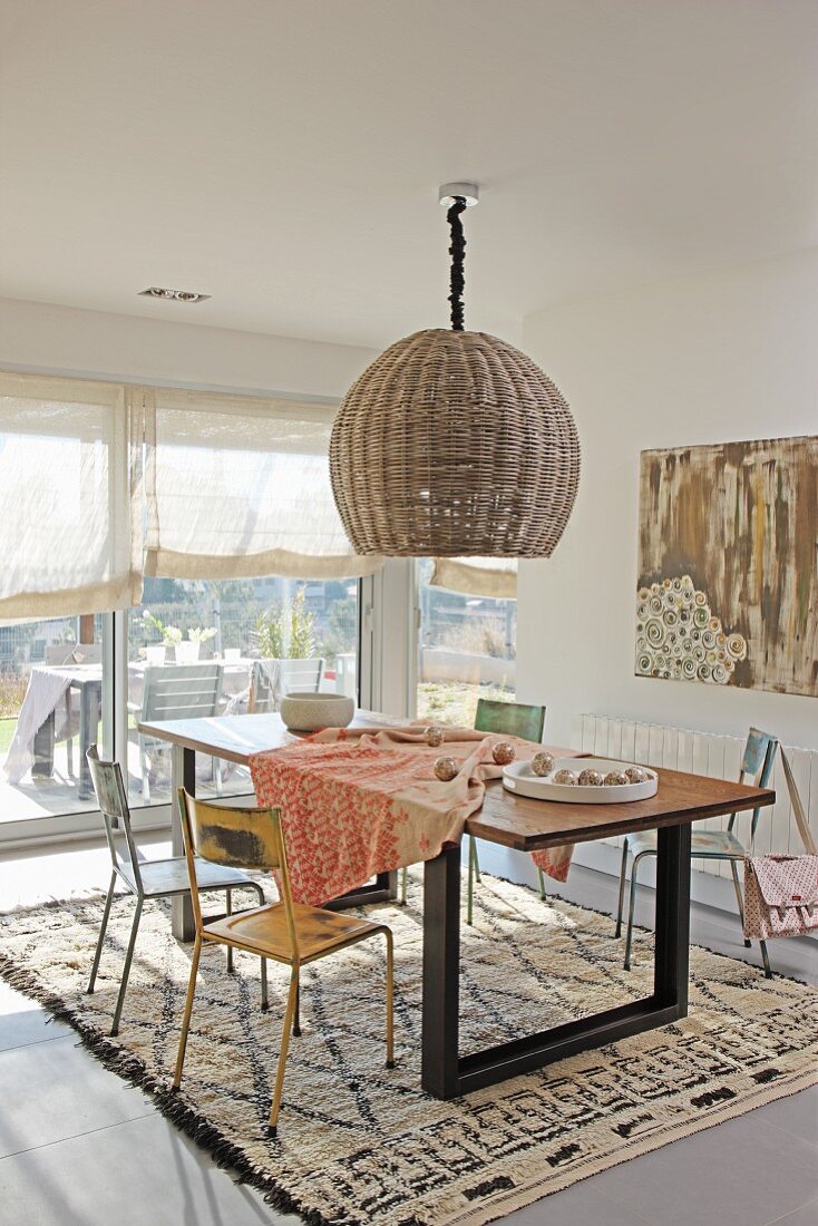 Pendant lamp with wicker lampshade above dining area with colourful, vintage metal chairs