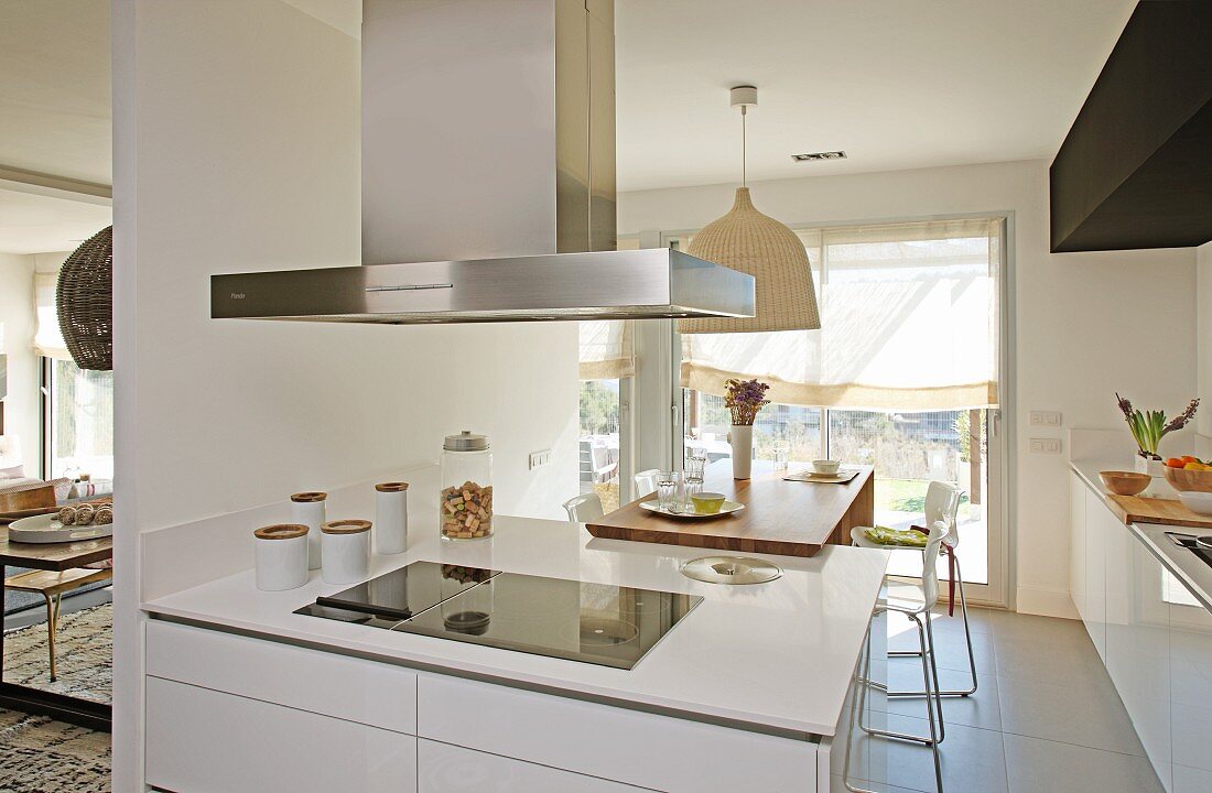 White kitchen counter with extractor hood in open-plan kitchen with dining area in background