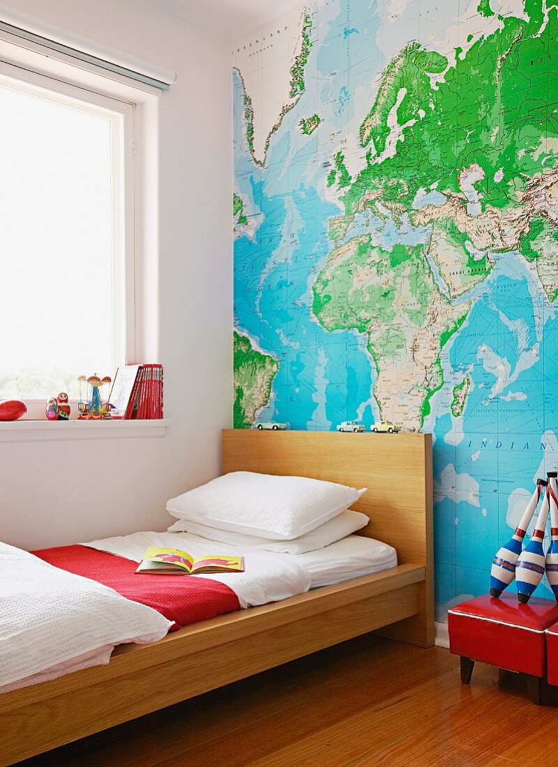 Single bed with wooden frame against wall with wallpaper map of world in child' bedroom