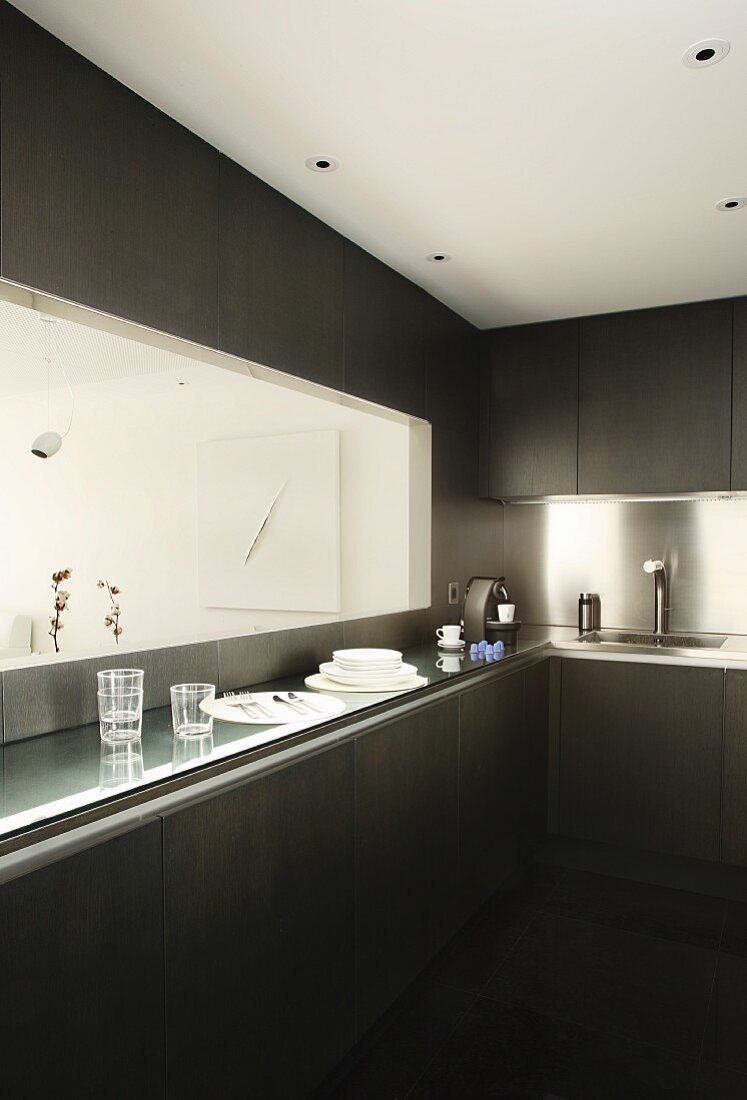 Designerküche mit dunklen Fronten und Edelstahl-Spritzschutz; Durchreiche über Ablagetheke mit Blick auf modernes Bild am Essplatz