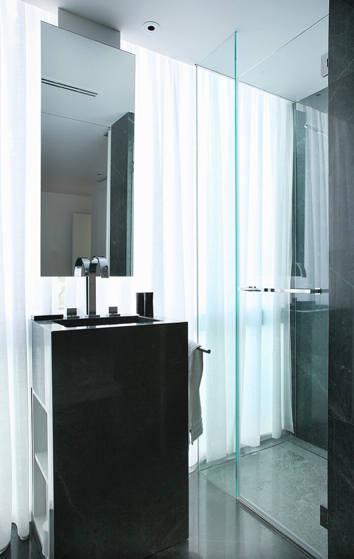 Waschtischsäule mit von Decke abgehängtem Spiegel und Duschkabine vor durchgehender Fensterfront mit Vorhang