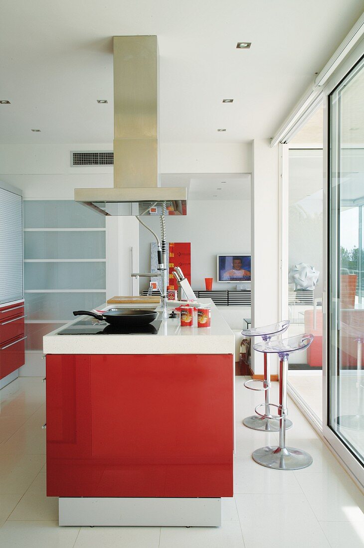 Kitchen island with red fronts and designer bar stools with plexiglas seats in front of sliding glass wall