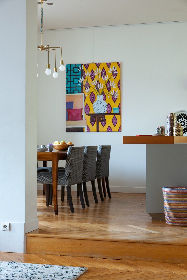Blick ins Esszimmer auf Stühle mit grauem Bezug am Tisch unter Art-Déco Pendelleuchte, im Hintergrund modernes Bild an Wand