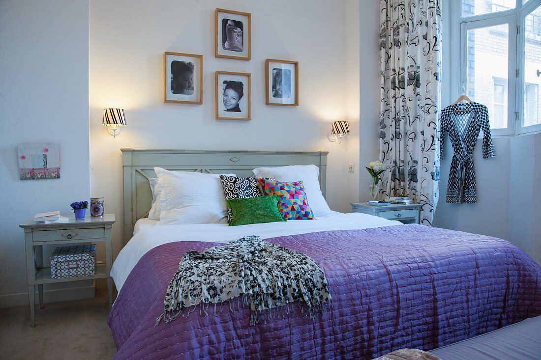 Violette Tagesdecke auf Doppelbett mit Holzkopfteil, an Wand gerahmte Fotos
