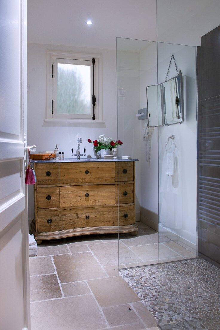 Blick durch offene Tür in Bad mit Landhauskommode, Duschkabine mit Kieselpflaster und Glasabtrennung