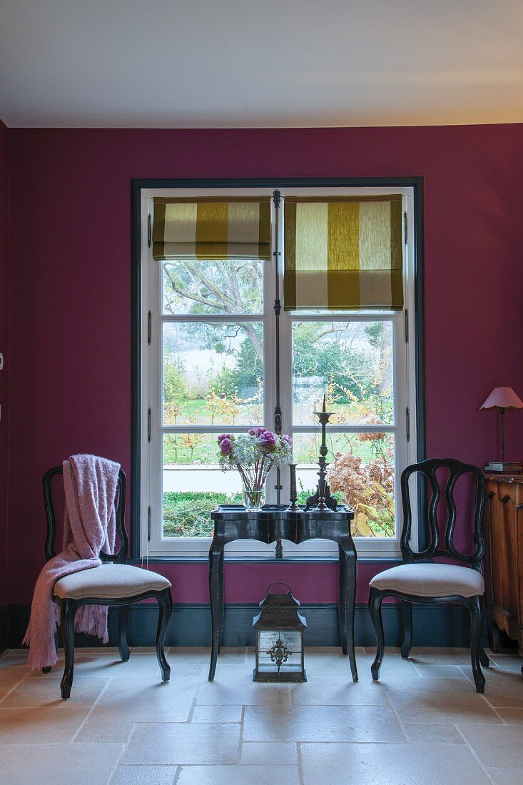 Zwei Stühle und Tisch vor lila getönter Wand und Fenster mit Faltrollo
